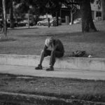 man in t-shirt and pants sitting on concrete floor in grayscale photography