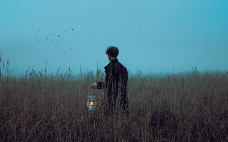 a man standing in a field holding a lantern