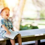 boy sitting on bench while holding a book