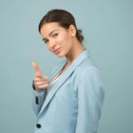 vain, A young woman in a blue suit exhibits confidence with a relaxed pose against a blue background.