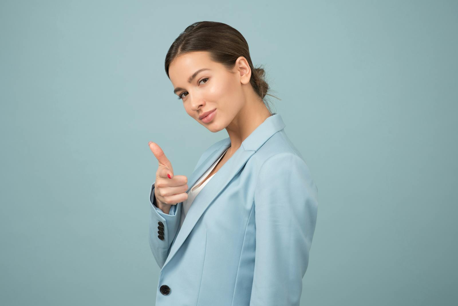 vain, A young woman in a blue suit exhibits confidence with a relaxed pose against a blue background.