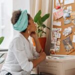 African American woman reflecting on a vision board by a window with plants.