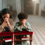 A mother and son kneeling and praying together inside a serene church.