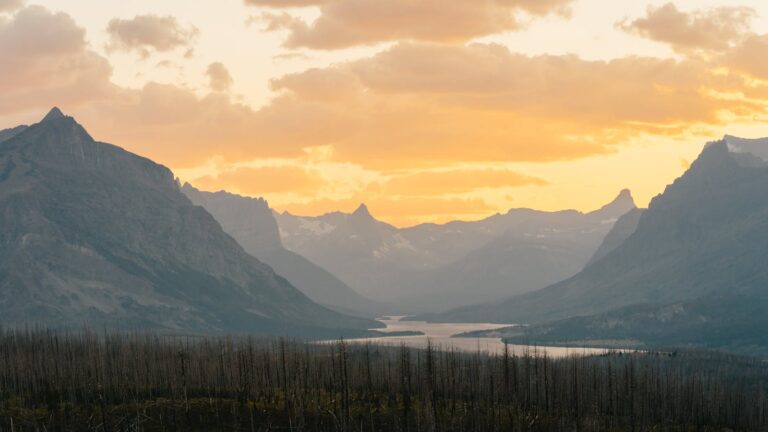 Vibrant sunrise at Glacier National Park, highlighting stunning mountain landscapes and serene river views.