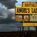 Old brothel sign, Angel's Ladies, under dramatic storm clouds in Nevada desert.