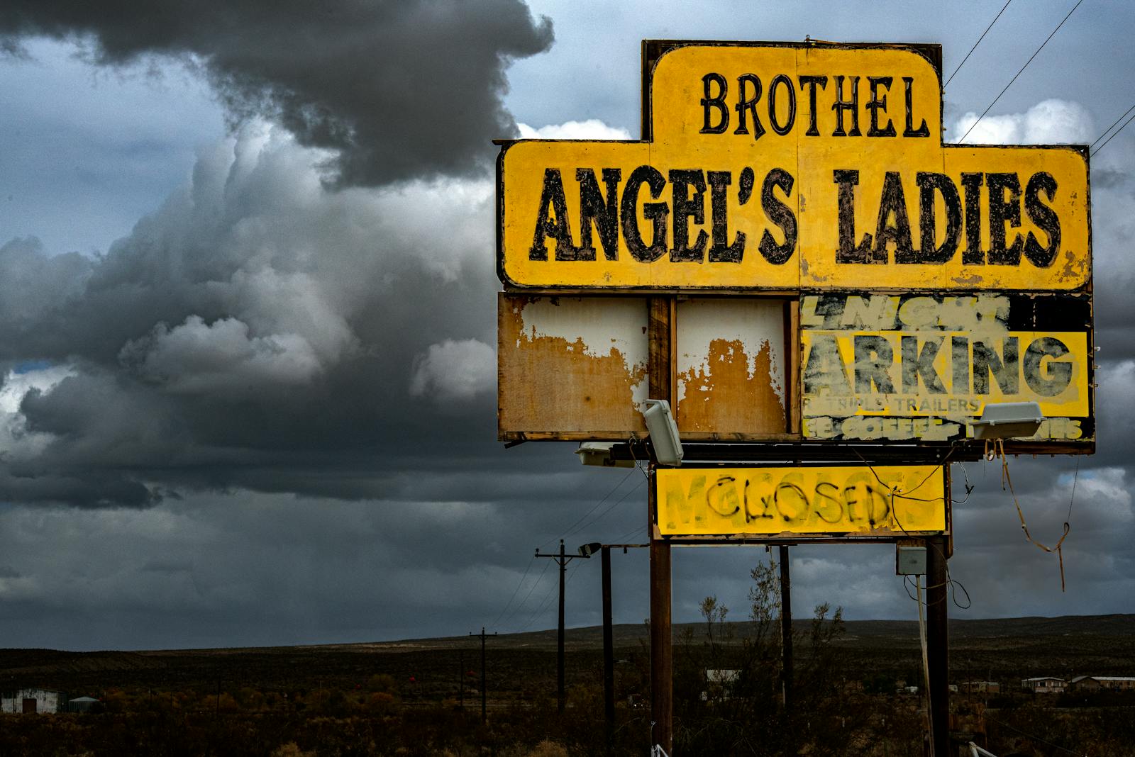 Old brothel sign, Angel's Ladies, under dramatic storm clouds in Nevada desert.