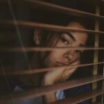 a woman looking out of a window with blinds