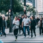 A diverse group of people crossing a street in a bustling city setting with skyscrapers.